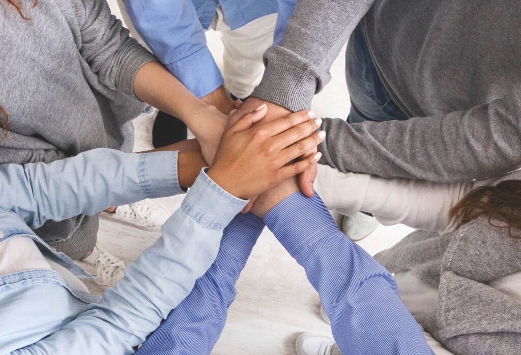 Gemeinschaft und Unterstützung in der Neuromentaltraining Ausbildung: Eine Gruppe legt ihre Hände vertrauensvoll aufeinander.